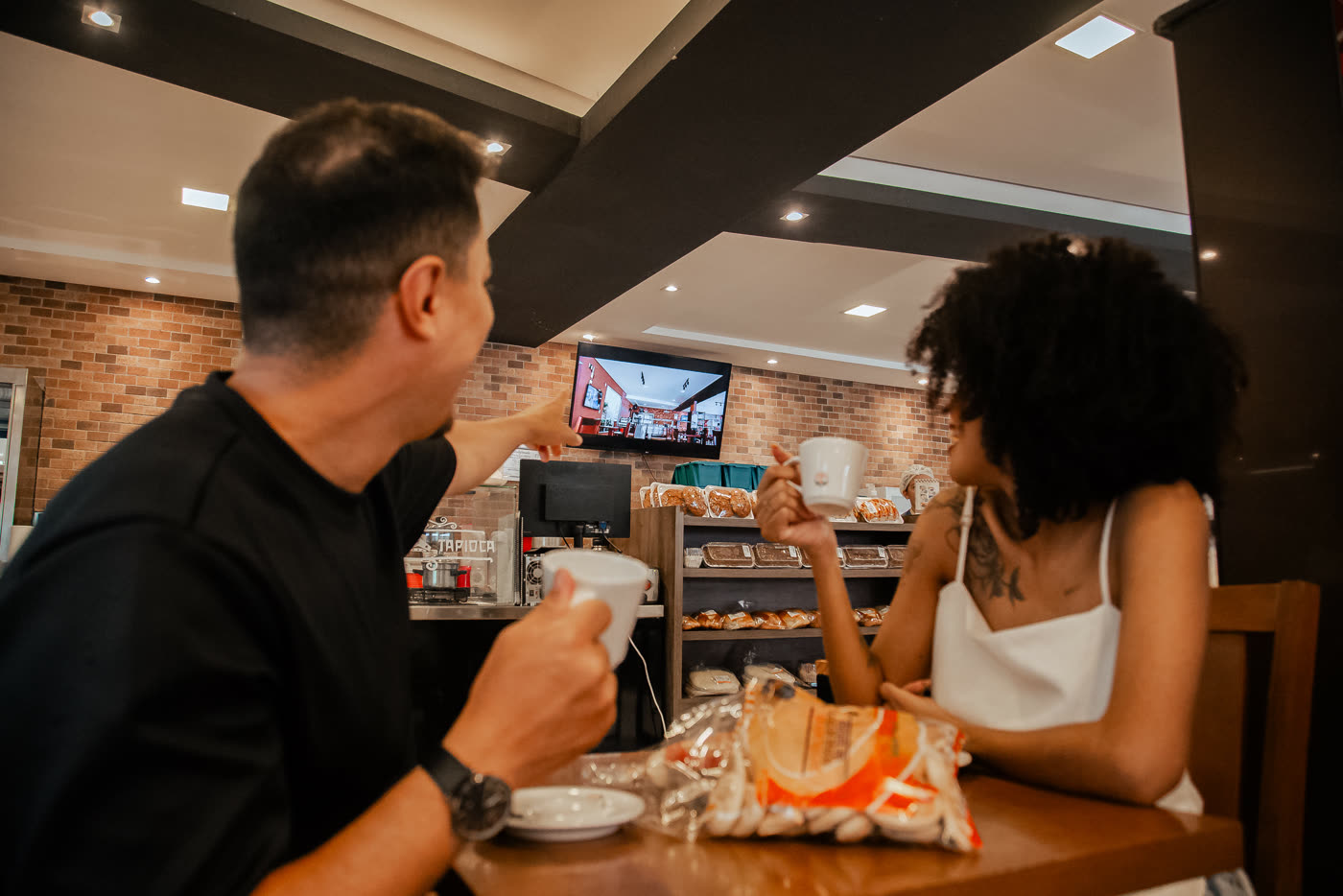 Casal tomando café com a tela do estabelecimento ao fundo