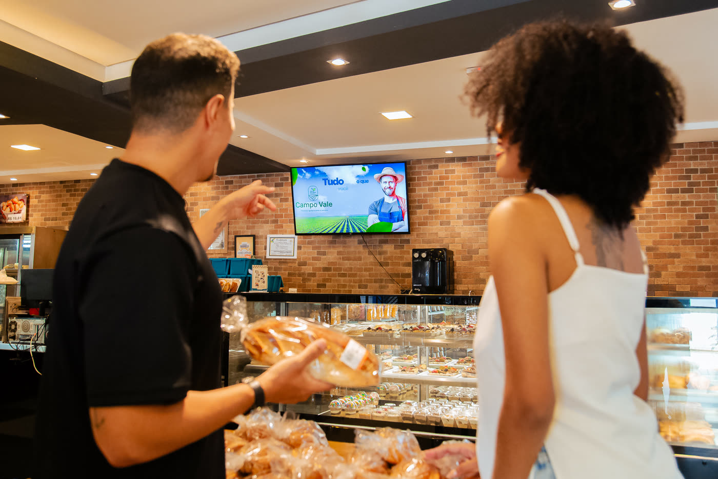 Clientes no balcão olhando para a tela do estabelecimento